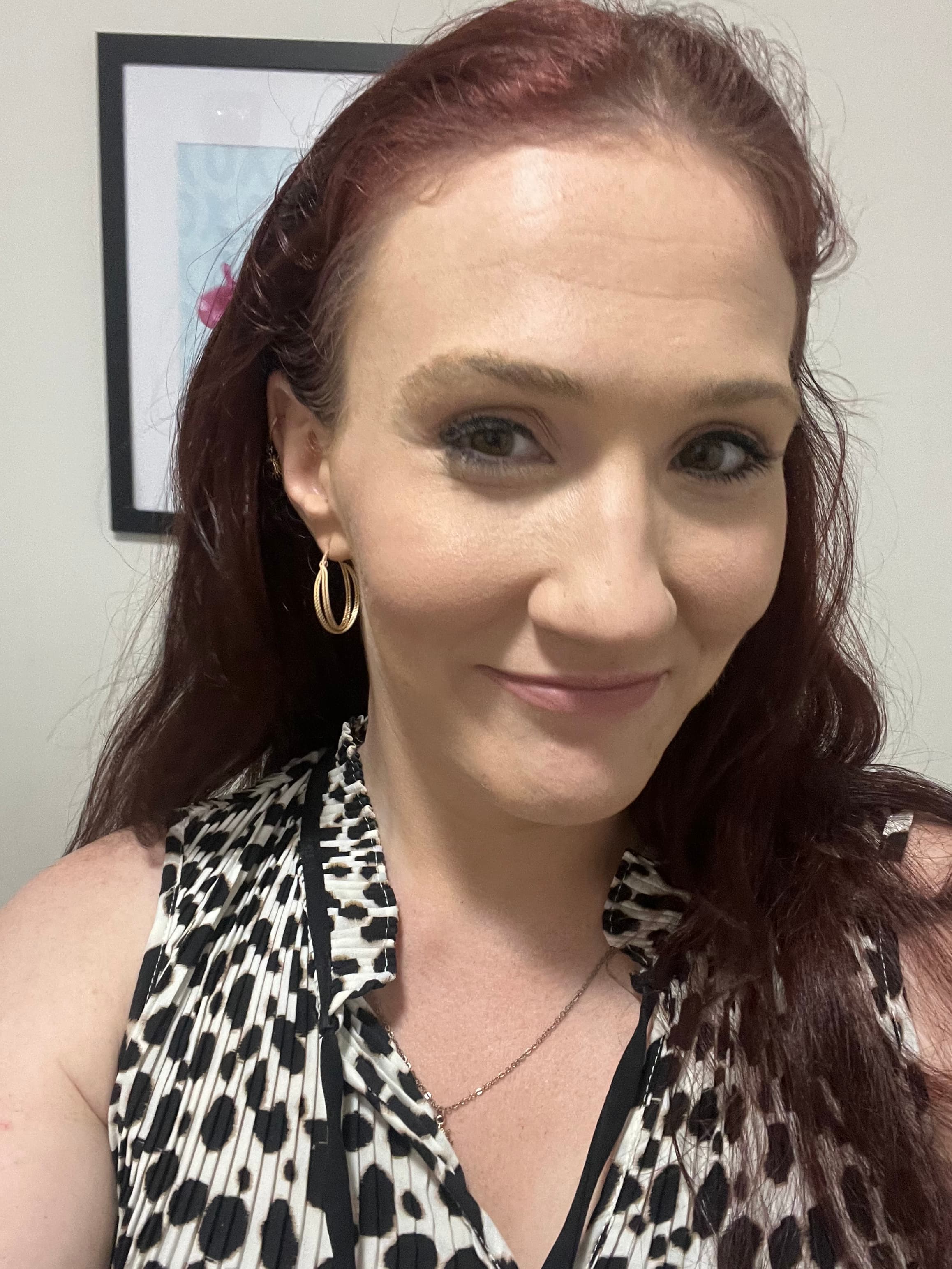 Smiling woman with long auburn hair wearing a black and white animal print sleeveless top.