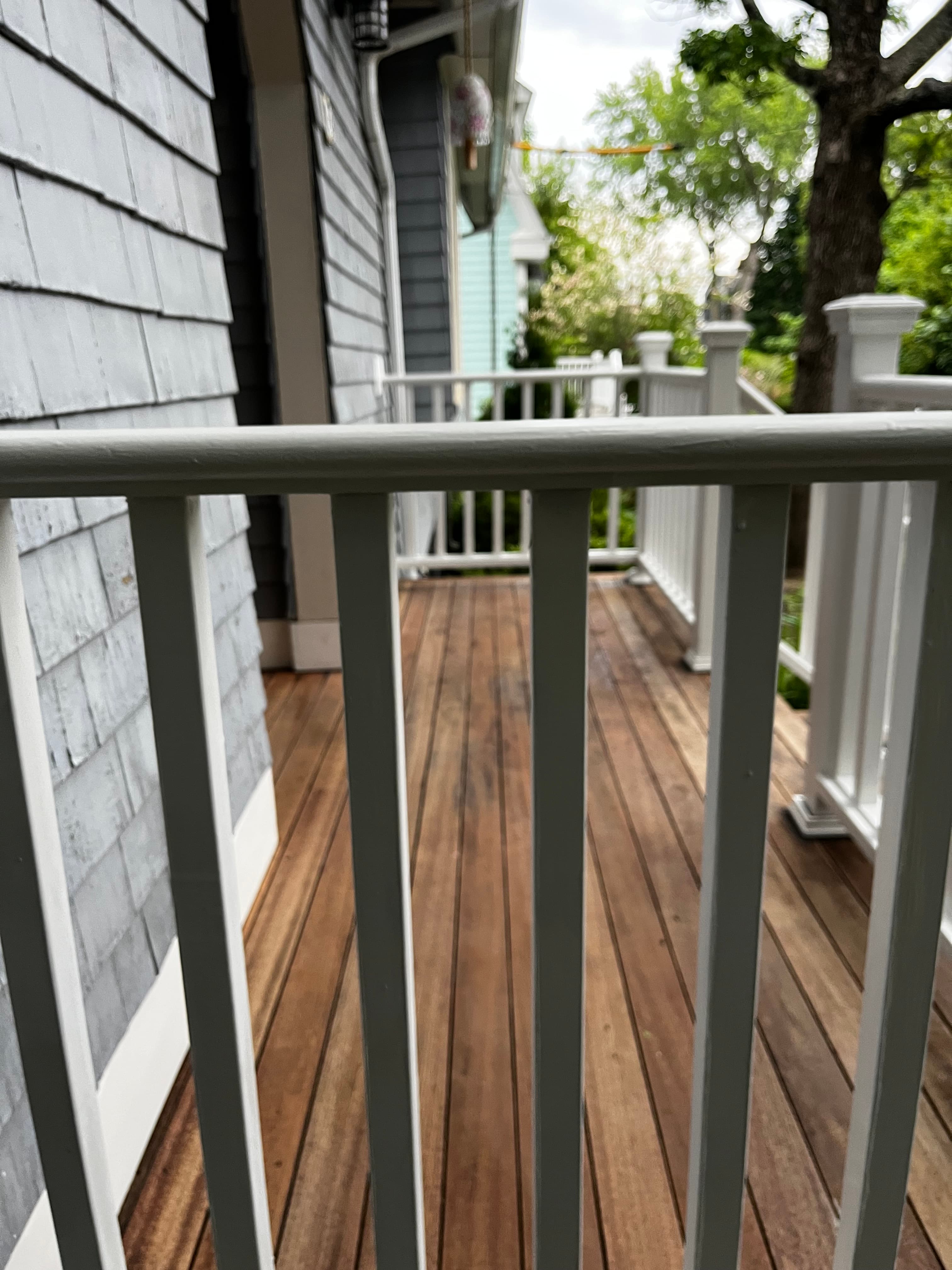 White wooden railing framing a brown planked deck floor next to a grey shingled house.